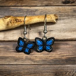 A pair of Lego blue and black butterflies with white dots on hook earrings handing off a branch on a wooden background