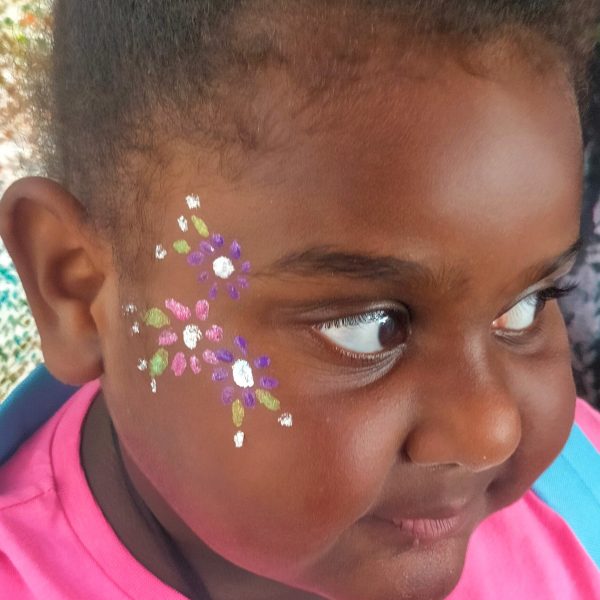 girl with sparkle flowers painted on her face with white, green and pink glitters