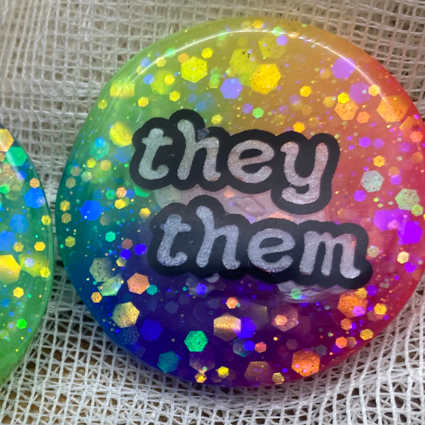 Glow in the dark rainbow pronoun badge with "any pronouns" label. Handmade in Melbourne by iridian.design.